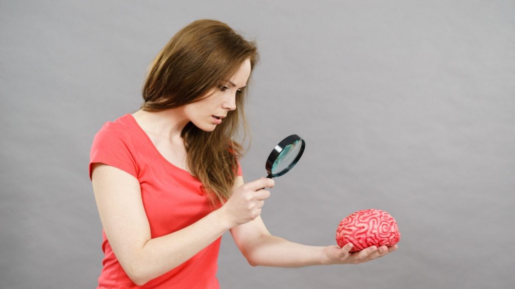 Kobieta przygląda się mózgowi za pomocą lupy. Tak obrazowo można opisać neurotrening.